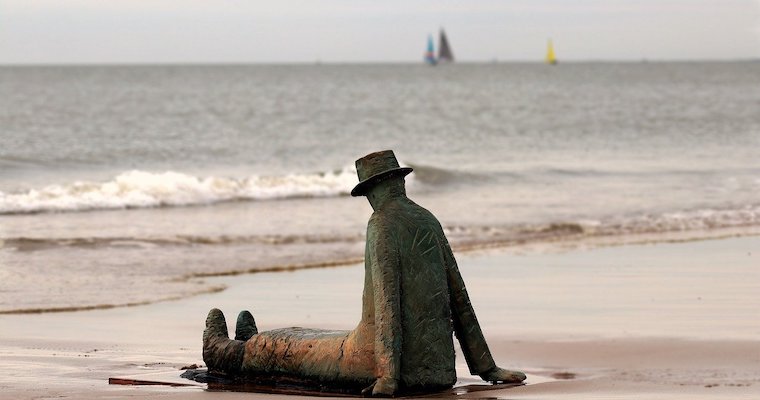 Un statue d'un homme assis sur la plage et regardant au loin.