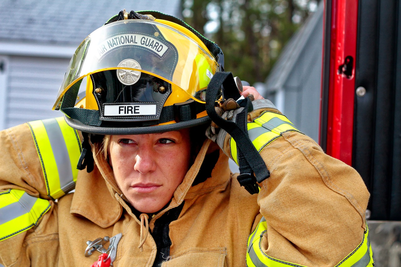 Femme pompière déjà vêtue de son vêtement ignifuge enfilant son casque